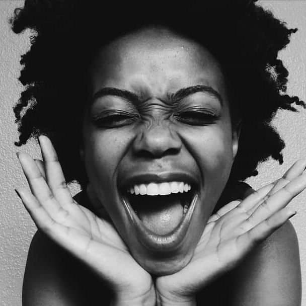 A woman with natural hair laughing, hands framing her face