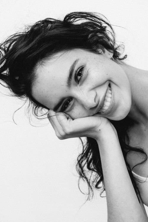A smiling woman with long wavy hair resting her head on her hand